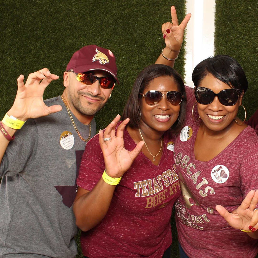 Three people at an alumni tailgate wearing Texas State merchandise smiling for a photo