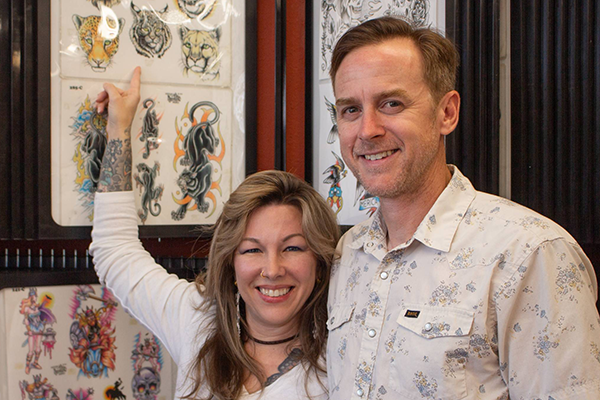 Morgan and Pat Egan at Classic Tattoo pointing at a Bobcat tattoo