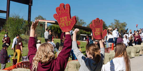 Students cheering at a Texas State soap box derby race with Texas State foam fingers
