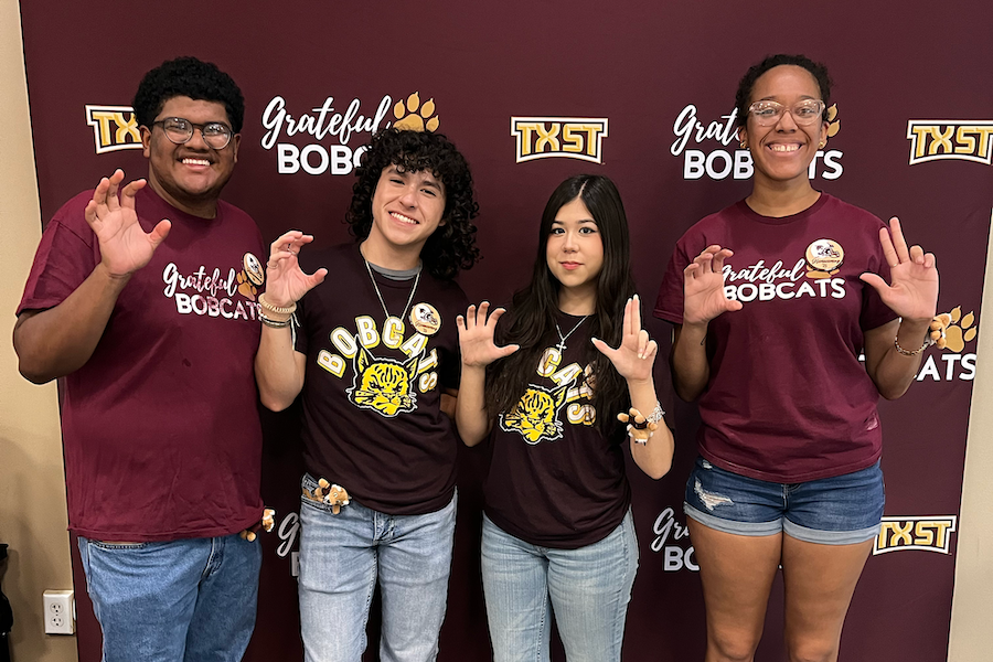 Four Texas State students in front of a Grateful Bobcats banner