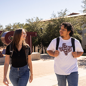Two students walking on campus next to the TXST sign