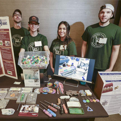 Four students standing behind table displaying their research