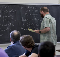 male math professor writing equations on chalk board
