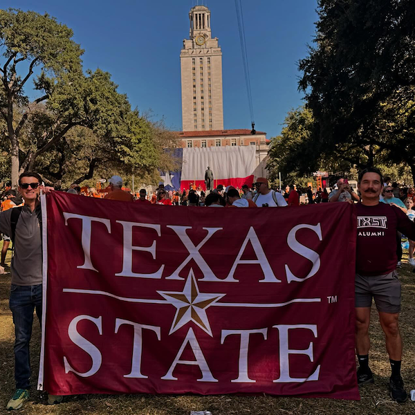 Two alums holding up a Texas State flag at College game day