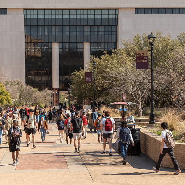 Students walking on campus in front of Alkek Library