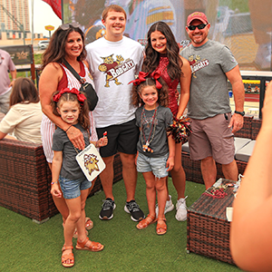 Group of three Bobcat fans with a Texas State cheerleader and two Bobcat kids at an alumni tailgate event